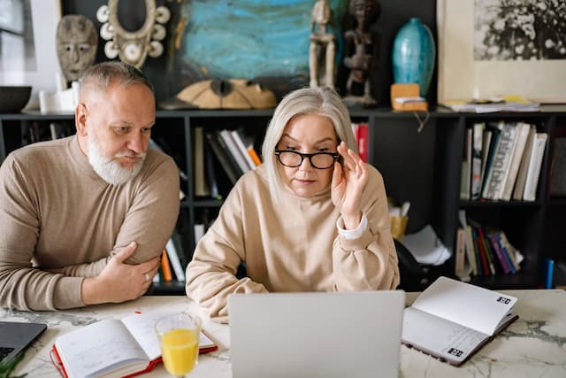 an elderly man and a woman are looking at a laptop screen