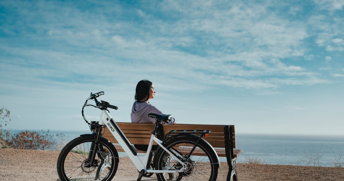 a girl is sitting on a bench next to an electric bike
