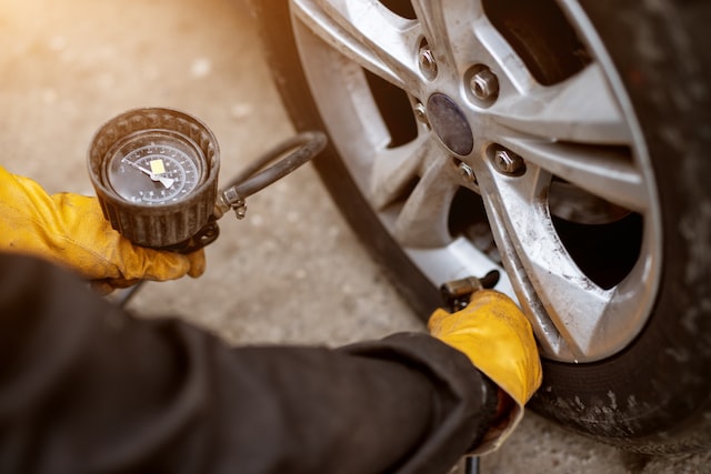 an experienced mechanic in orange gloves is placing air valve on a car wheel preparing to pressurize it