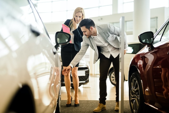 a man and a woman inspect a car before buying