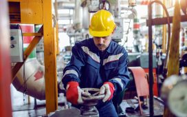 plant worker in working suit and with protective helmet on head screwing valve