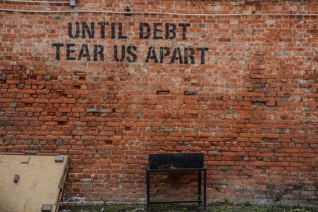 until debt tear us apart printed red brick wall