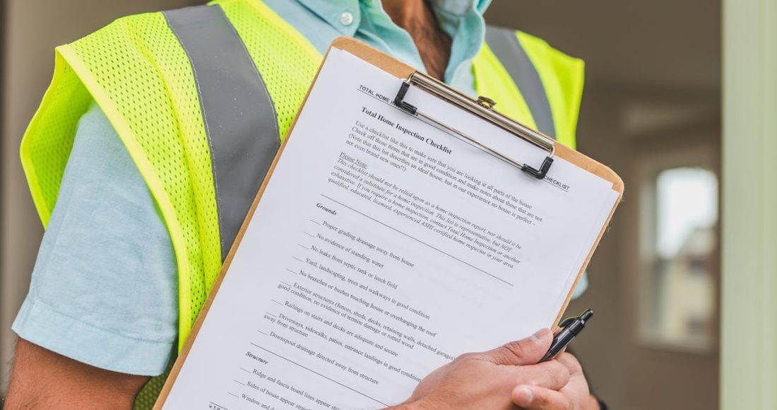 person-in-yellow-reflective-safety-vest-holding-a-pen-and-checklist-of-house-inspection