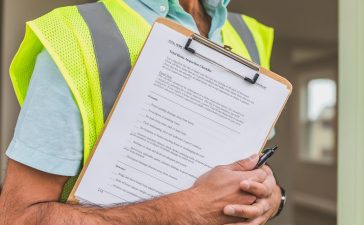 person-in-yellow-reflective-safety-vest-holding-a-pen-and-checklist-of-house-inspection