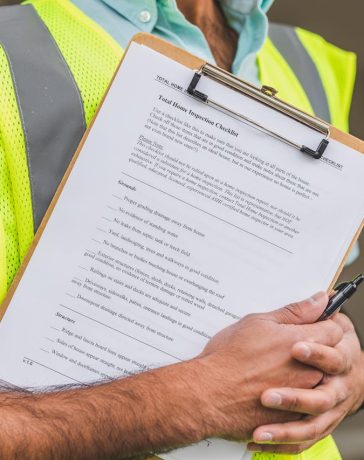 person-in-yellow-reflective-safety-vest-holding-a-pen-and-checklist-of-house-inspection