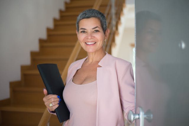 an-elderly-woman-holding-a-folder-while-standing-on-the-doorway