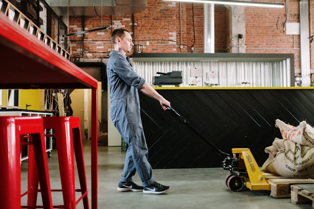 man-in-blue-denim-jacket-and-blue-denim-jeans-holding-black-and-yellow-hand-truck